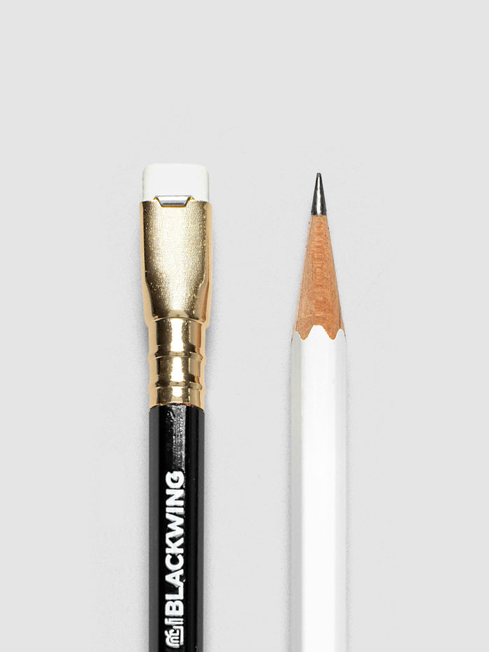 A close-up studio shot of the eraser end of the black Blackwing pencil and the sharpened point end of the white Backwing pencil on a light gray background.