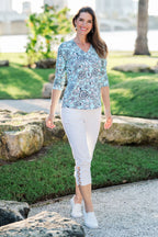 Woman wearing a patterned blue top and white pants standing outdoors.