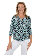 Woman wearing a patterned blouse with white pants on a white background.