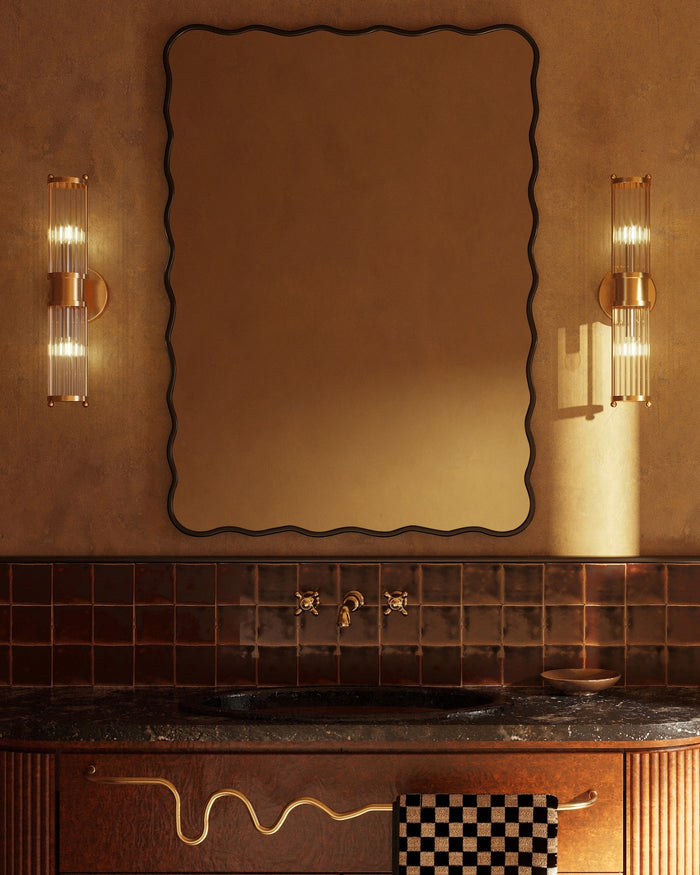 Rectangular wall mirror with a black frame and softly wavy edges, mounted above a bathroom vanity between two wall sconces.