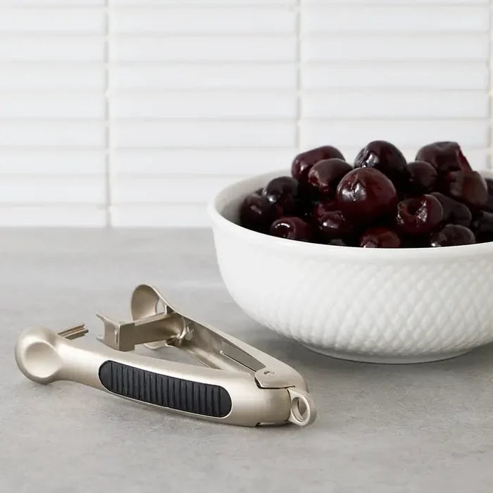 A cherry pitter with cherries in a bowl on white background.