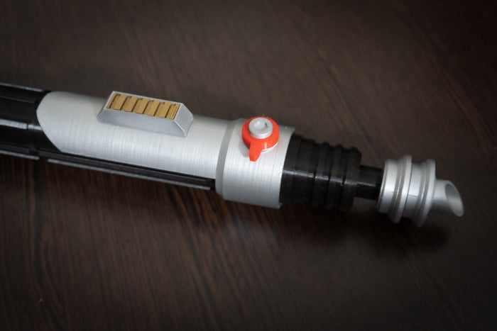 Ezra Bridger second lightsaber hilt cosplay prop in silver and black with red button detail on wooden surface