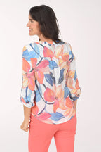 Woman wearing a colorful floral blouse and coral pants on a white background