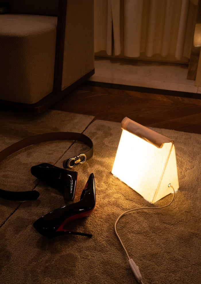 High heels, belt, and small lamp on a carpeted bedroom floor.