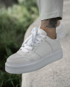 Martin Valen men's high sneakers in white, outdoor side close-up worn on foot beside greenery showing embossed logo and perforated toe