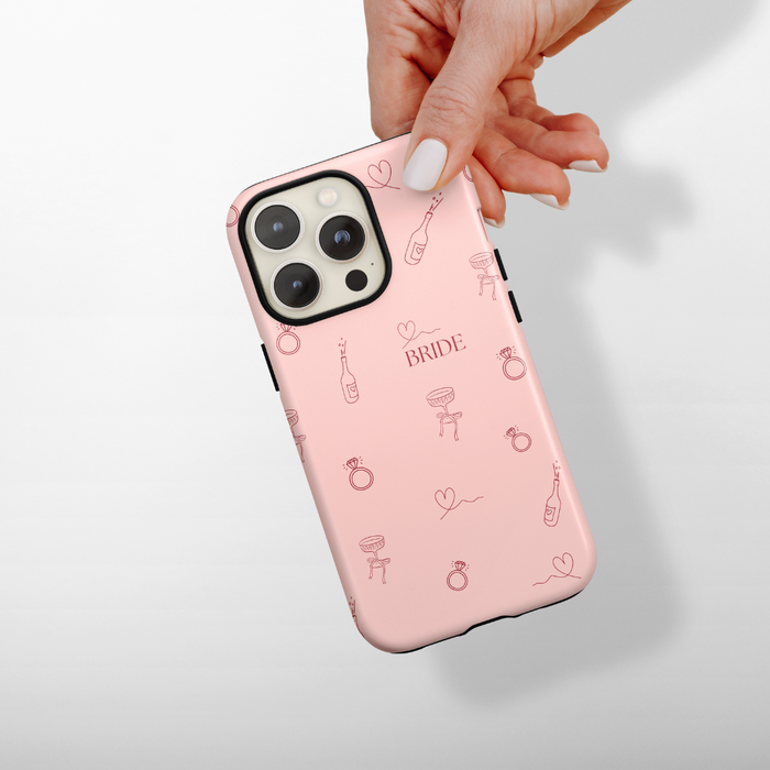 Blush pink Coconut Lane bridal phone case with BRIDE and wedding motifs, held in a hand.