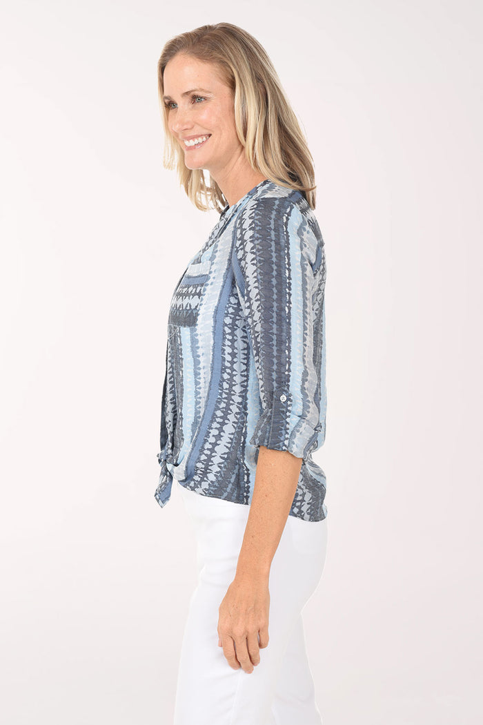 Woman wearing a blue patterned blouse and white pants on a white background