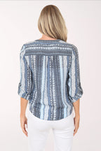 Woman wearing a blue patterned blouse and white pants on a white background