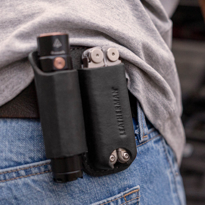 Black leather belt sheath holding a multitool and flashlight on a person’s hip