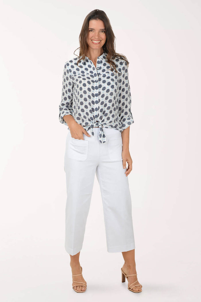 Woman wearing a patterned blouse and white pants on a white background