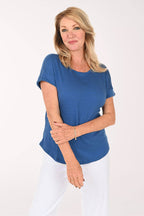 A woman modeling a short-sleeve blue top with white pants against a plain white studio background.