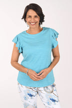 Woman wearing a light blue ruffled blouse with floral pants on a white background