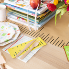 Children's table setting with books, cutlery, and a mug on a wooden surface.