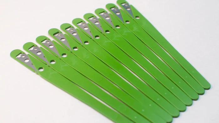 10 green bread lame blades with the protectors still on splayed out next to each other on white background.