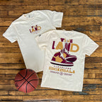 Two white t-shirts with 'The Land' and basketball graphics on a wooden surface, accompanied by a basketball.