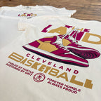T-shirt with 'The Land Cleveland Basketball' design featuring a sneaker graphic on a wooden surface.