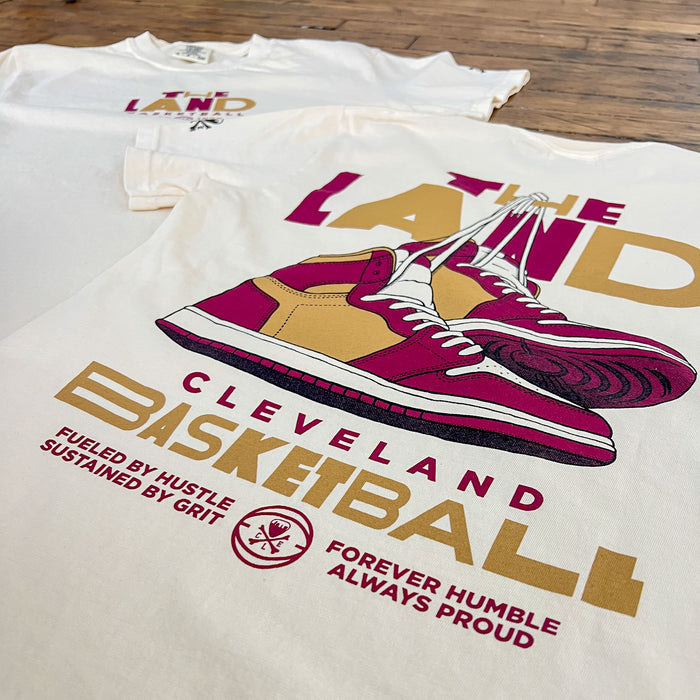 T-shirt with 'The Land Cleveland Basketball' design featuring a sneaker graphic on a wooden surface.