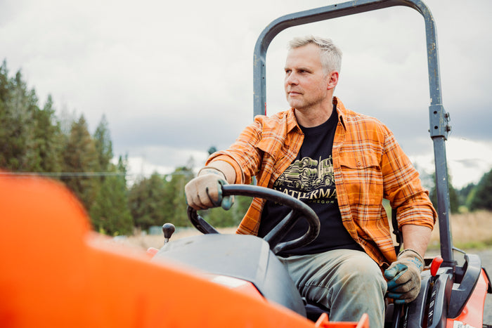 A person wearing a black Leatherman Timber Tee driving a tractor outdoors.