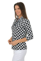 Woman wearing a black and white patterned blouse with white pants on a white background. Side shot.