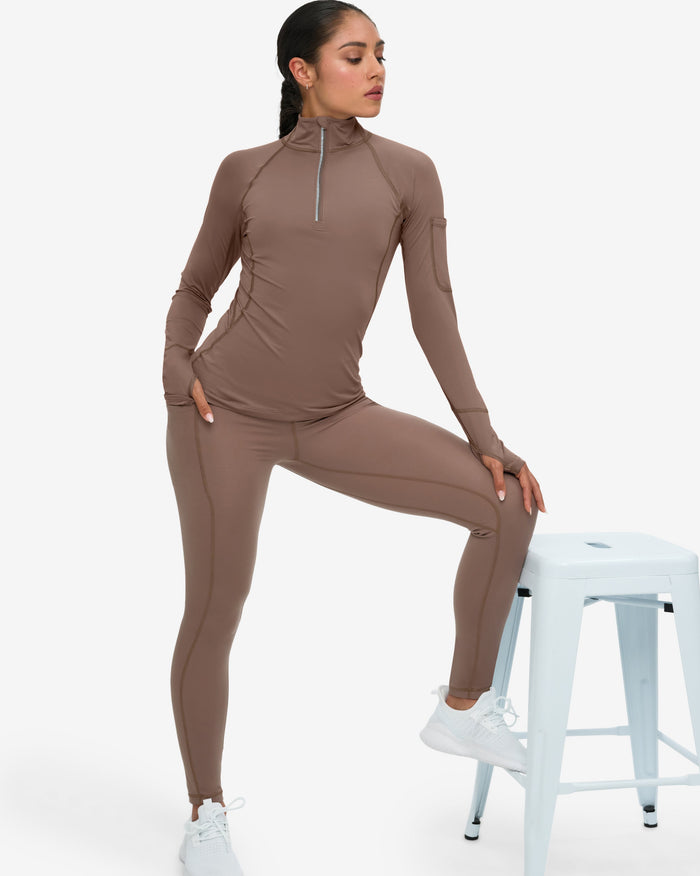 Woman wearing a brown athletic outfit sitting on a white stool against a white background