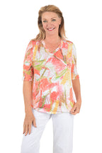 Woman wearing a colorful floral blouse and white pants on a white background.