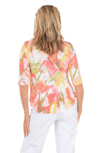 Woman wearing a colorful floral blouse and white pants on a white background. Back shot.